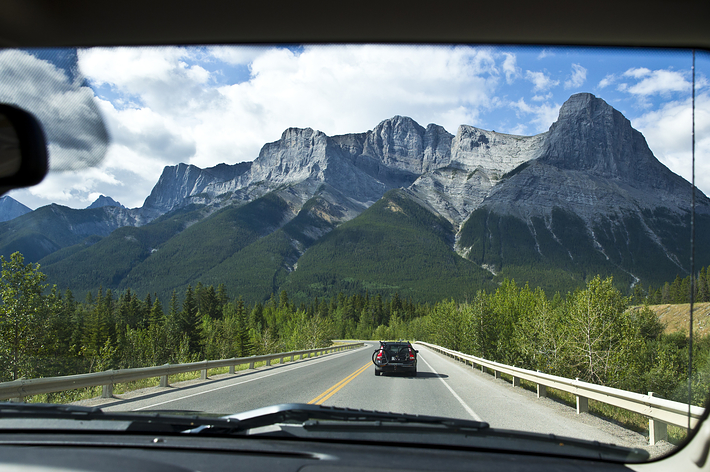 車の車窓から見た広大な山脈と前方の道路の風景。