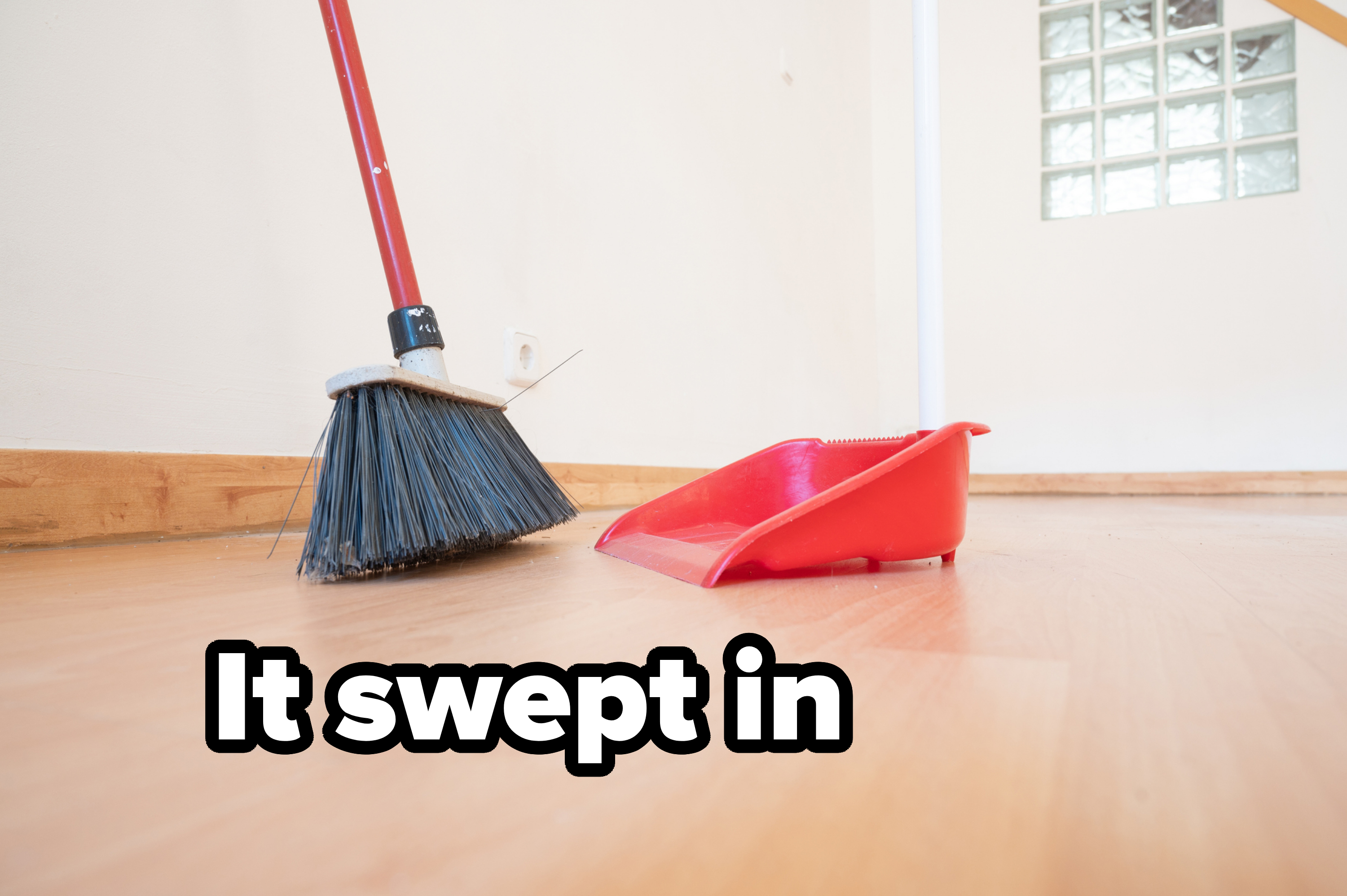 A broom and a red dustpan on a wooden floor in a clean, indoor setting