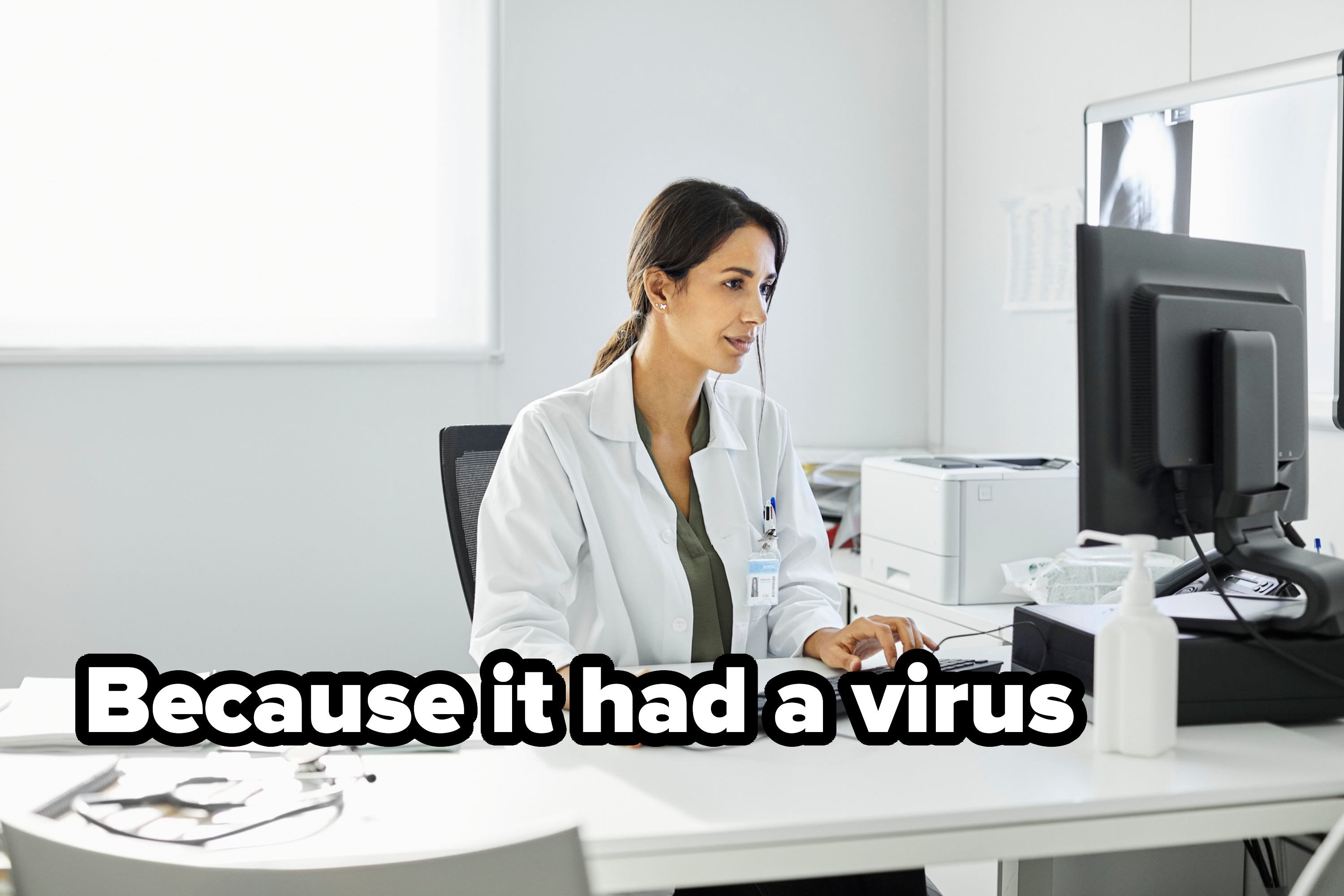 A person in a lab coat works at a computer desk in a bright office, focusing on the screen