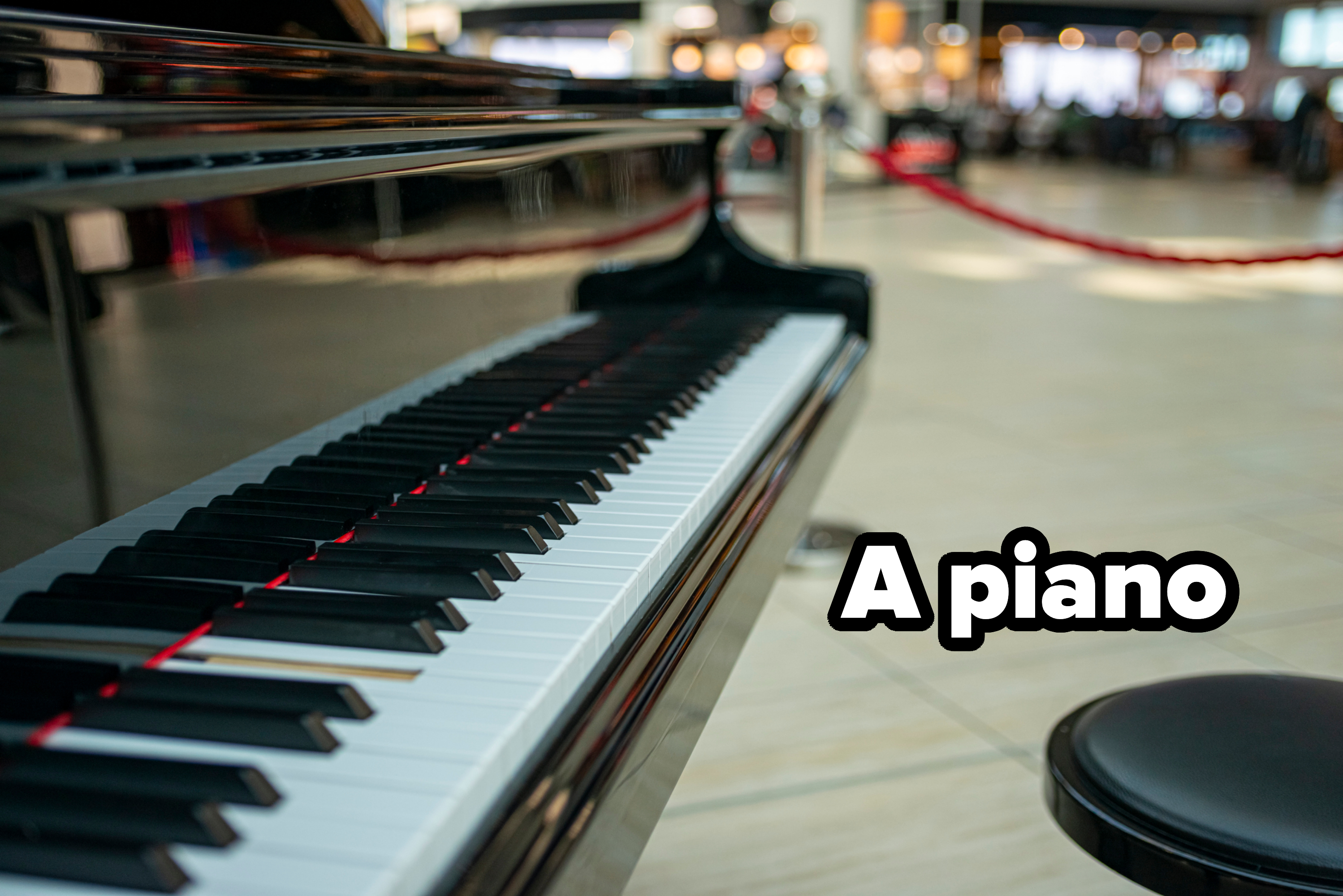 Close-up of a grand piano keyboard with a blurred background, featuring red rope barriers in a public space