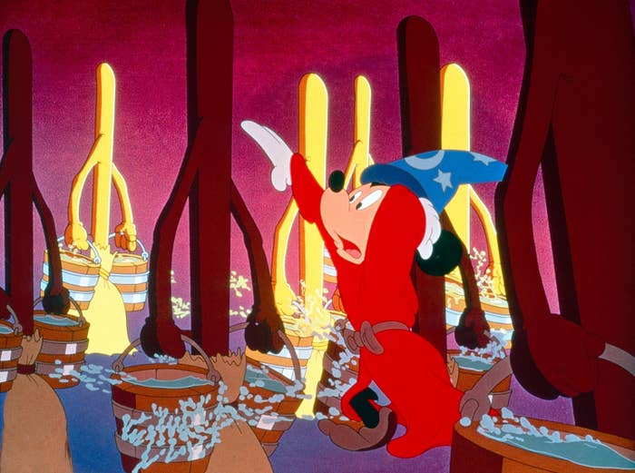 Mickey Mouse in a wizard hat and red robe controls enchanted brooms carrying water buckets in a scene from 