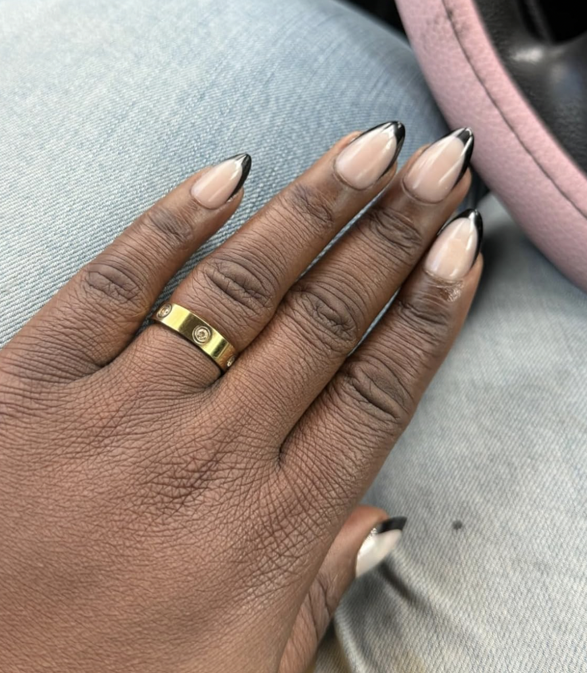 A hand with stylish long nails featuring black tips and a gold ring with a small diamond on the ring finger