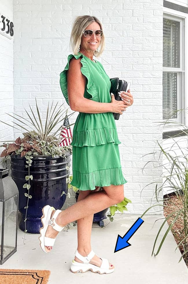 Woman successful a stylish ruffled tiered formal and achromatic sandals stands connected a porch, accessorized with sunglasses and a achromatic clutch