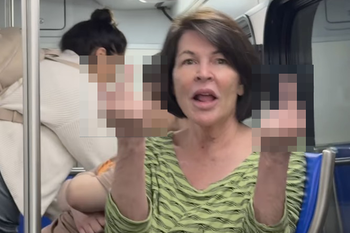 女性が公共交通機関で両手で中指を立てている。周囲に他の乗客もいる。