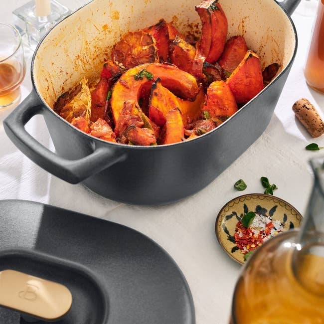 Cast robust  Dutch oven filled with roasted squash and herbs, accompanied by a vessel  of olive lipid  and tiny  sheet  with spices connected  a achromatic  tablecloth