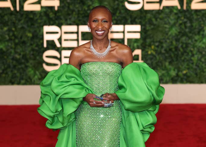 Person wearing an elegant, off-shoulder gown with ruffled sleeves on a red carpet, holding an award