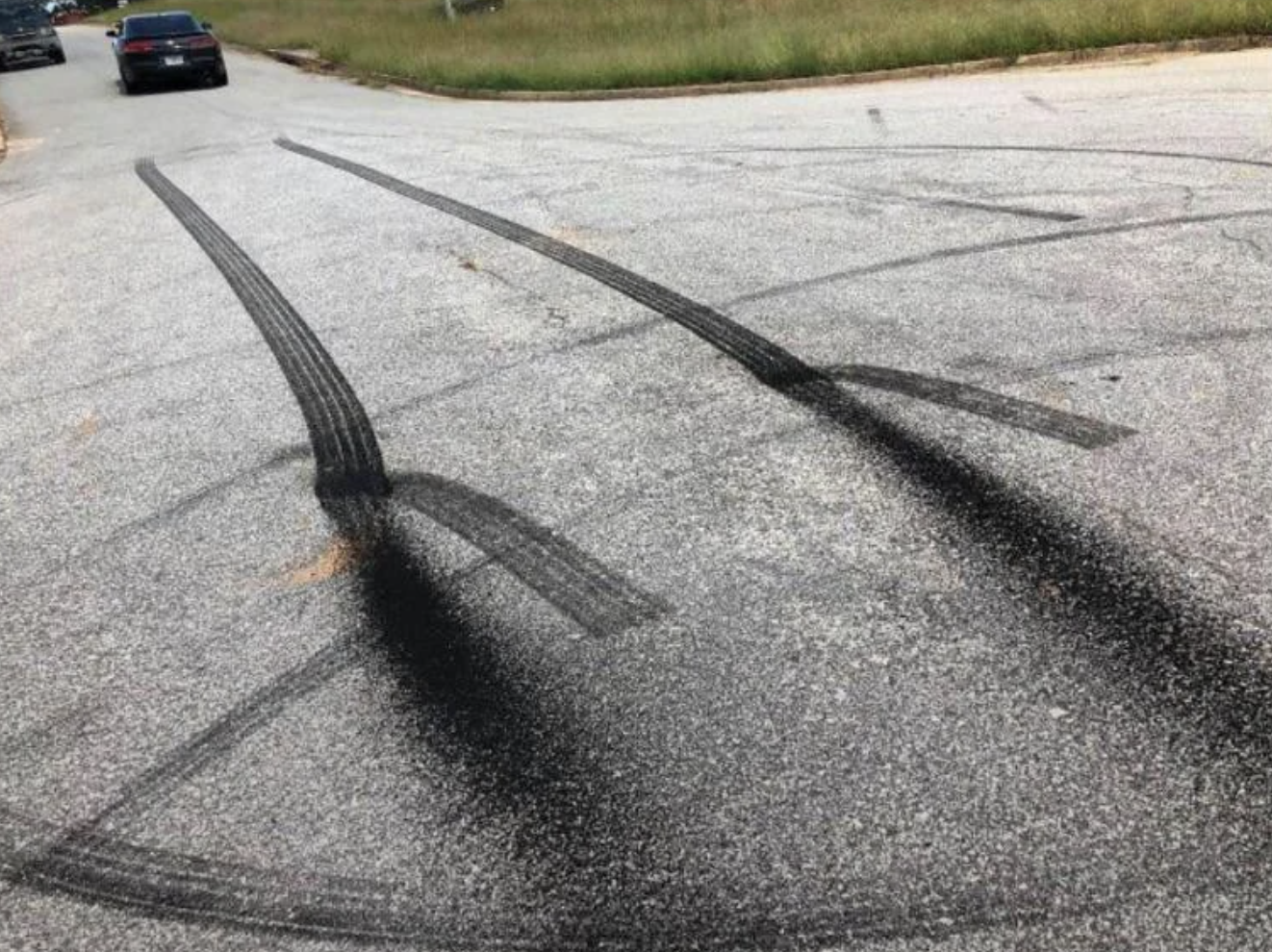 Tire marks on a quiet road, with a car driving away in the background
