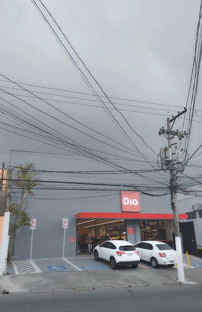 Grocery store named "Dia" with parking spaces out front and overhead power lines. Cloudy sky in the background