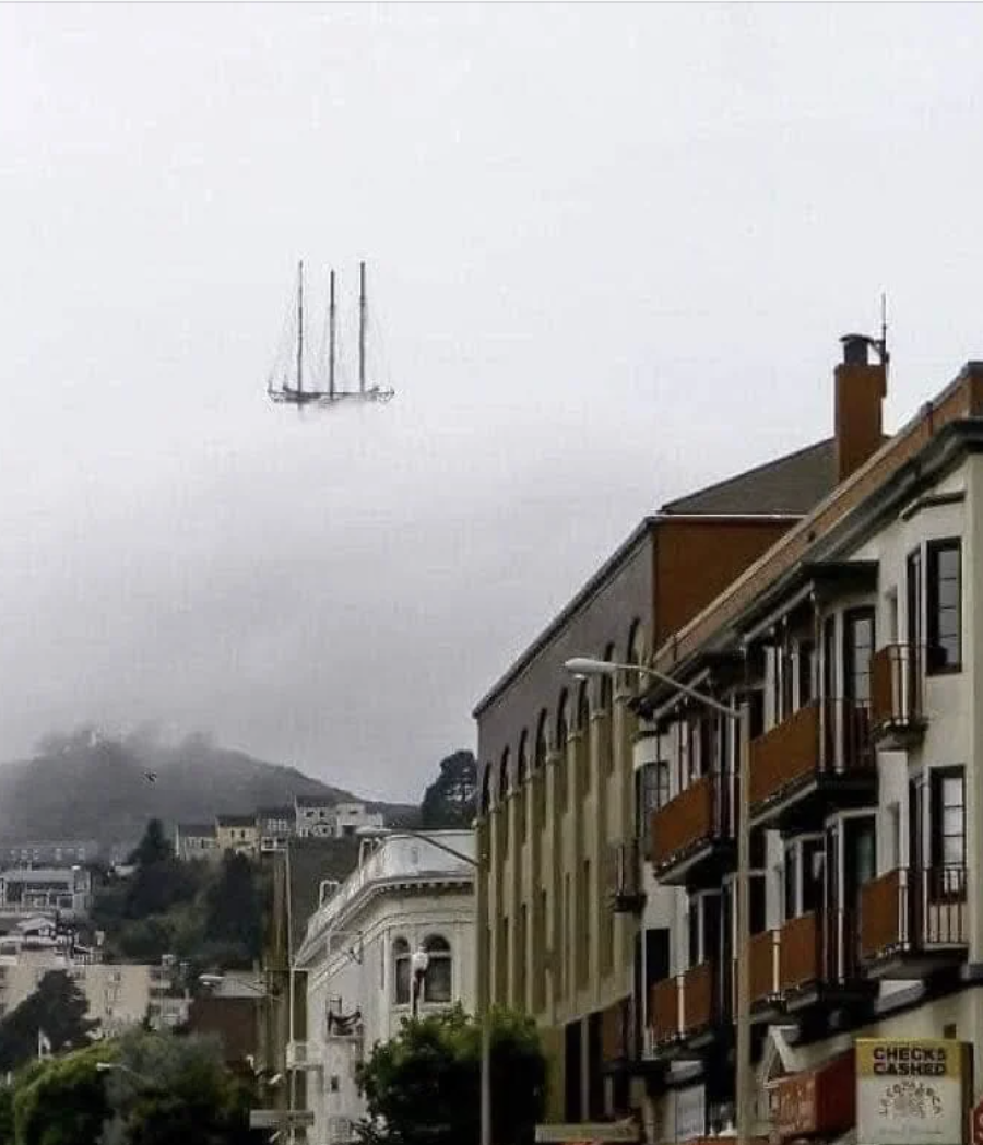 Optical illusion of a ship appearing to sail in the sky above a cityscape with buildings in the foreground