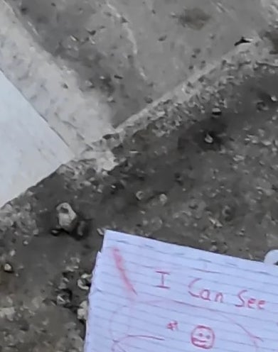 A torn piece of lined paper on concrete reads &quot;I can see you&quot; with a small drawn face