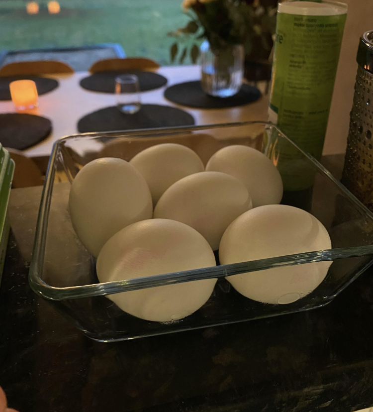 Six eggs in a glass dish on a dark table, with a softly lit dining area in the background