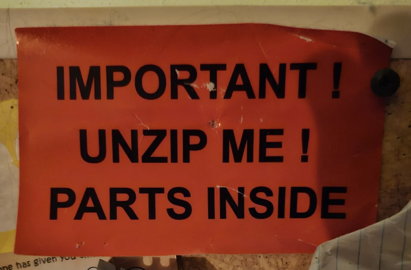 Sign on a bulletin board reads: "IMPORTANT! UNZIP ME! PARTS INSIDE."
