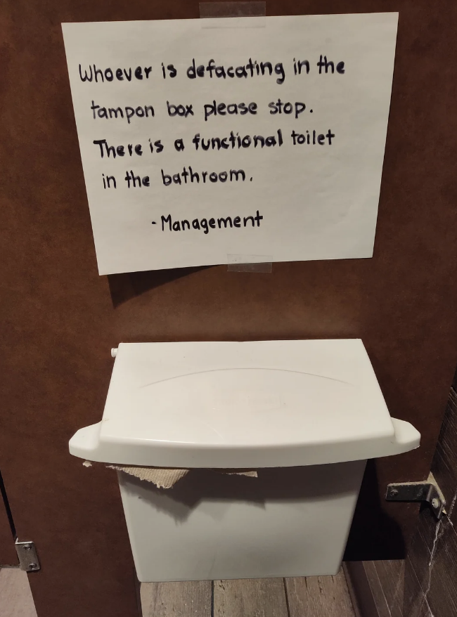 Sign on restroom stall reads: "Whoever is defecating in the tampon box please stop. There is a functional toilet in the bathroom. - Management"