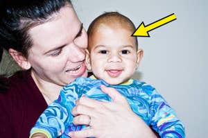 A person smiling and holding a baby, who is also smiling. A yellow arrow points to the baby's head