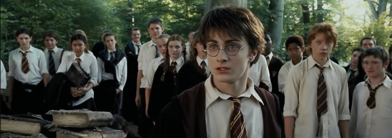 Scene from a fantasy film with a young person in a school uniform and glasses, surrounded by peers in a forest setting, looking concerned