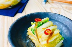 器に盛られたピリ辛風味の野菜の漬物。背景に箸とガラスの器に入った追加の漬物が見える。