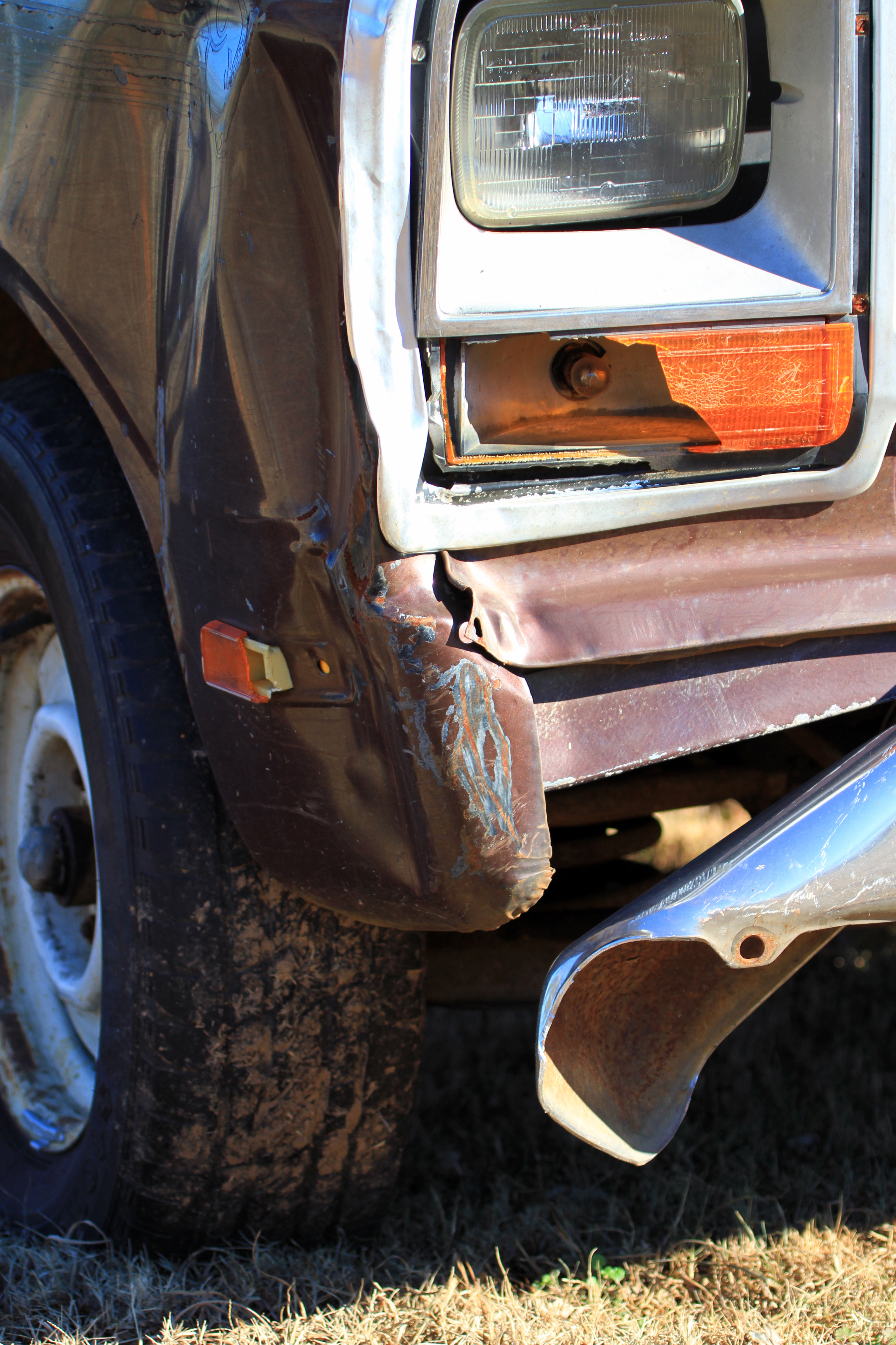 Front corner of a damaged vehicle with a dented bumper and headlight frame, showing minor collision impact