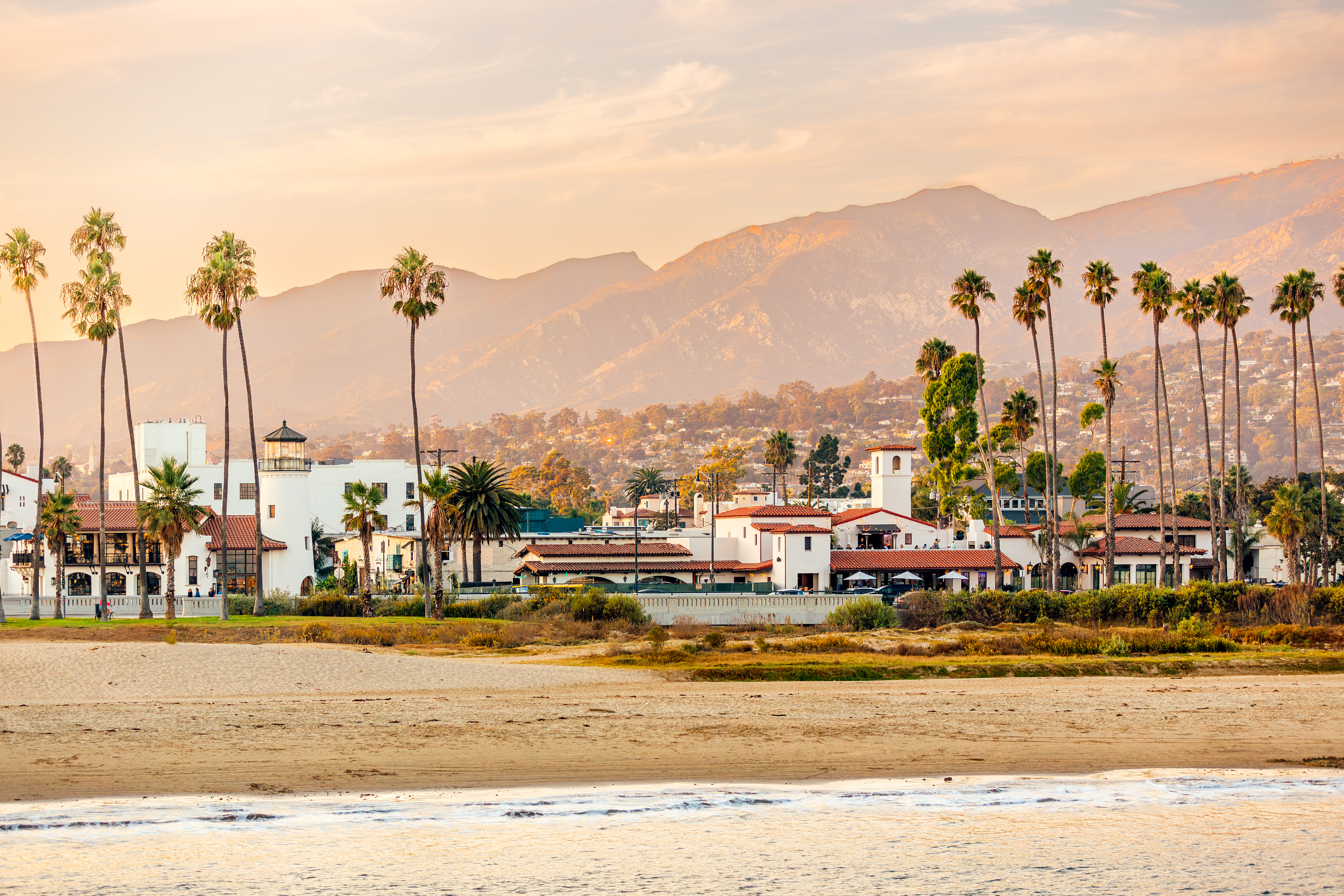 Beachfront area with palm trees, Spanish-style buildings, and mountains in the background