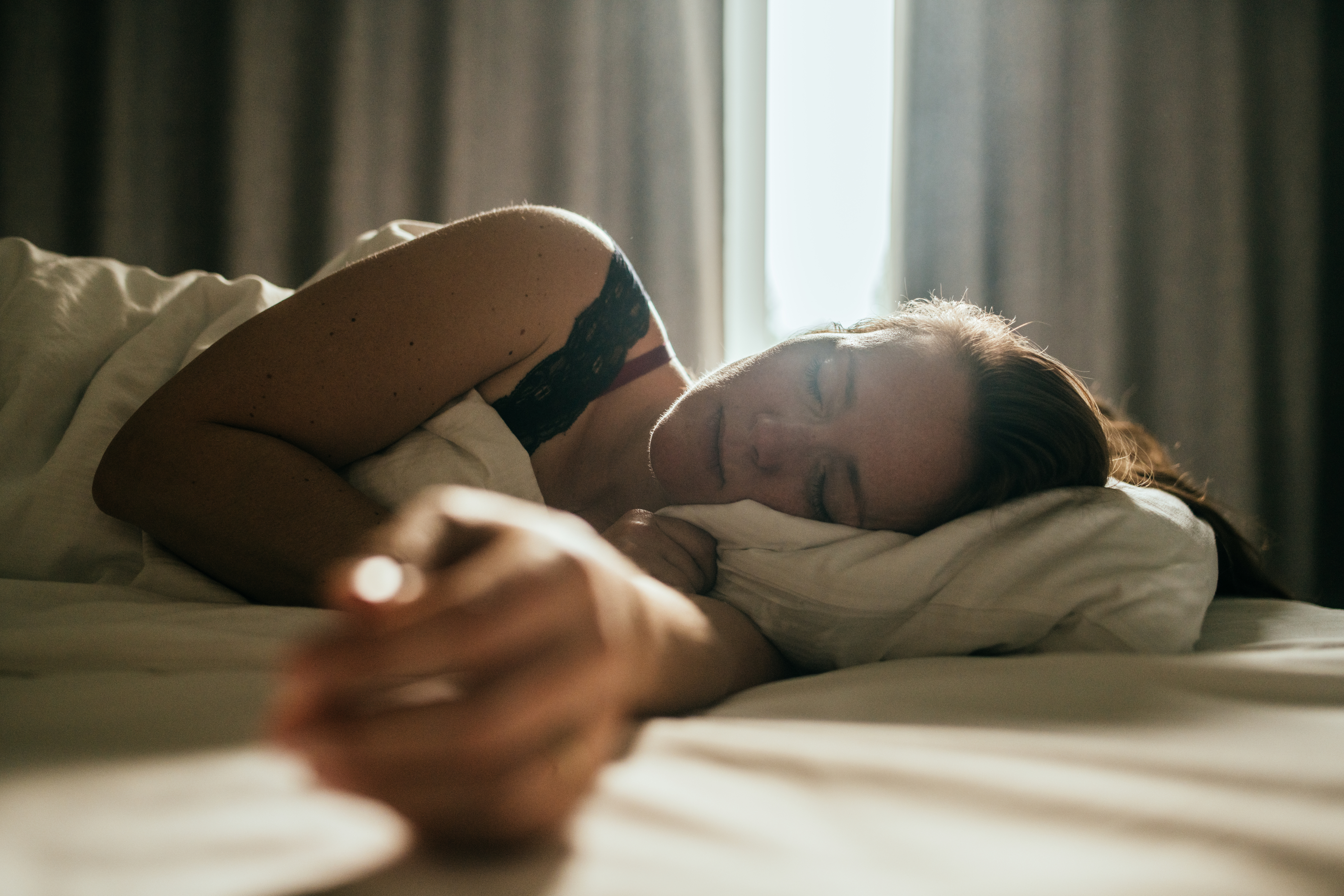 Person sleeping peacefully in bed with sunlight filtering through curtains