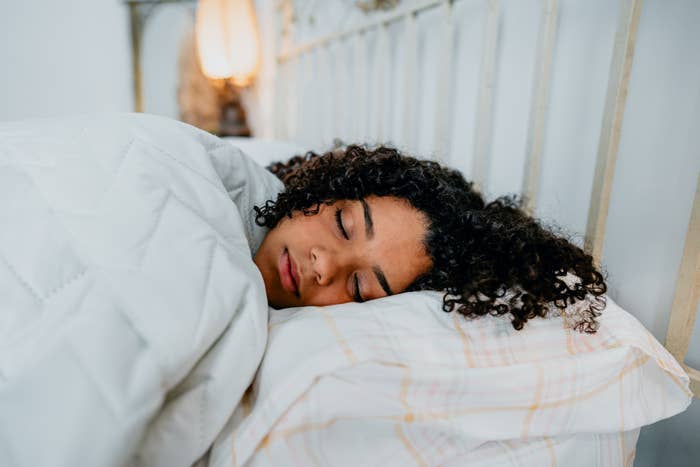 Person peacefully sleeping in bed with a cozy blanket and soft pillow, highlighting a restful sleep environment