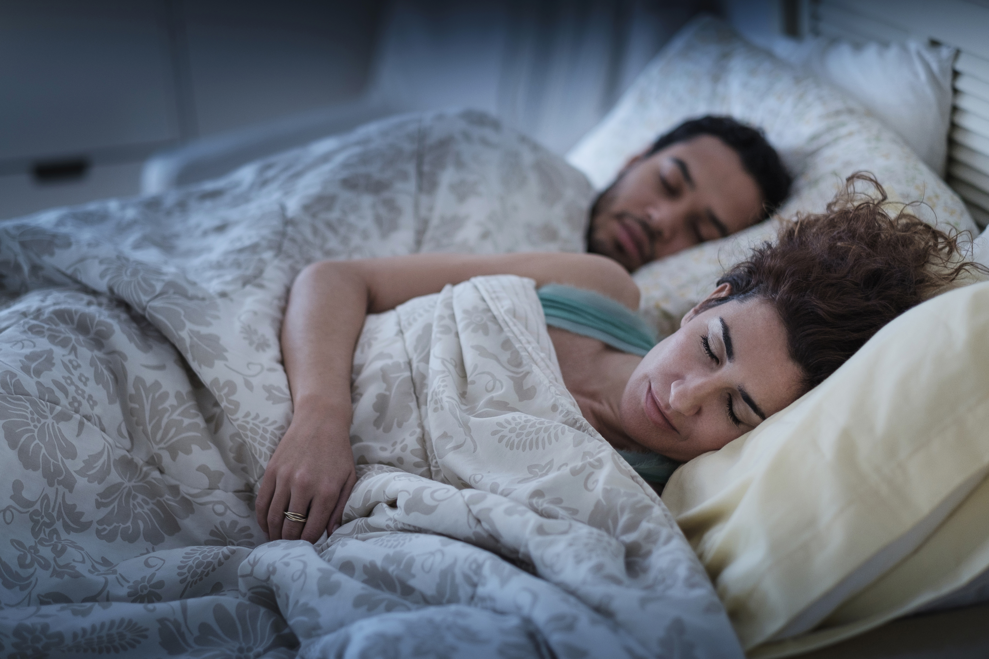 A couple peacefully asleep in bed, covered with patterned blankets, conveying a sense of rest and relaxation