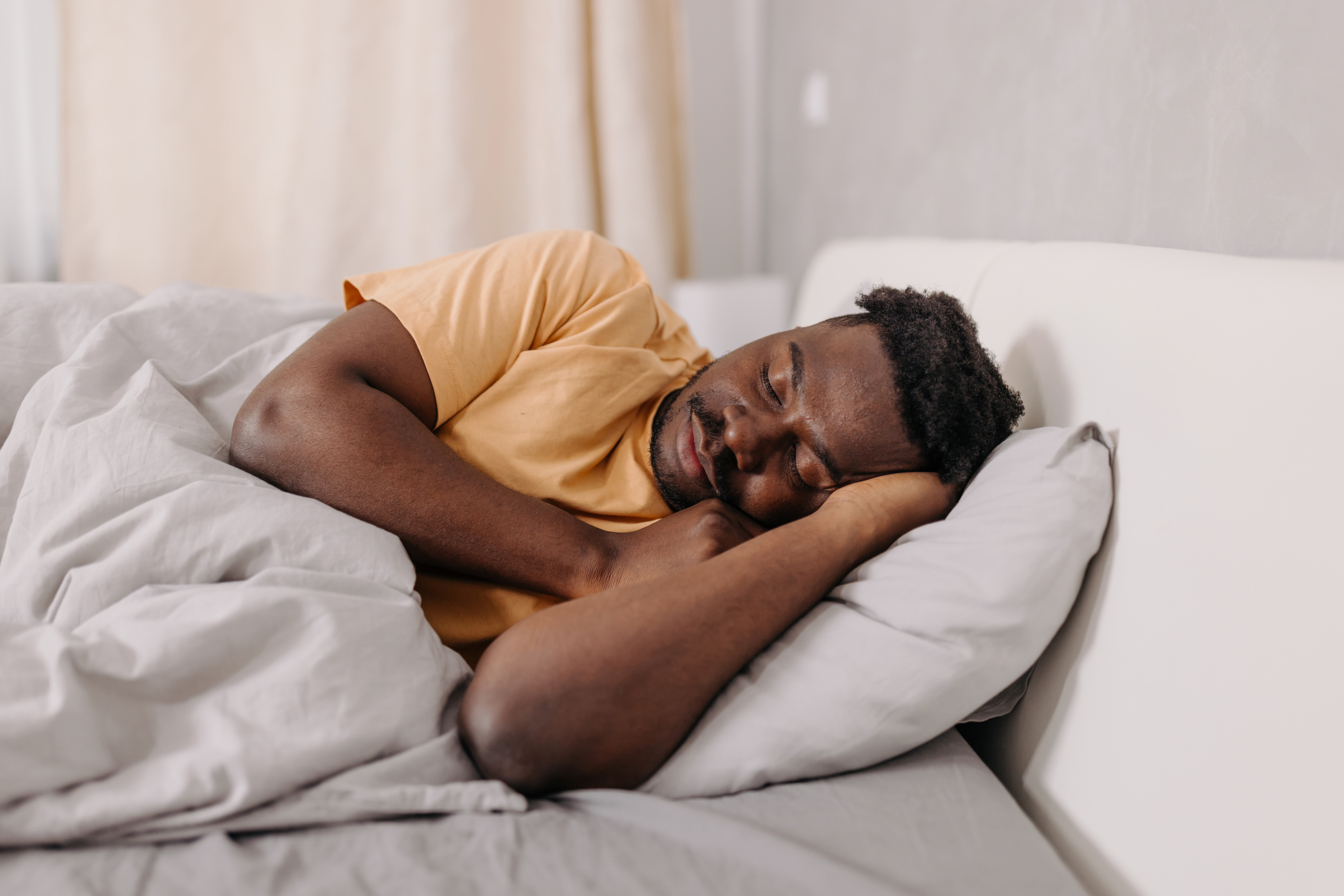 Person peacefully sleeping in bed, lying on their side with head resting on a pillow, wrapped in a cozy blanket