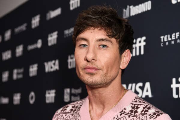 Barry Keoghan on the red carpet in patterned sweater at a celebrity event, posing in front of media logos and sponsors