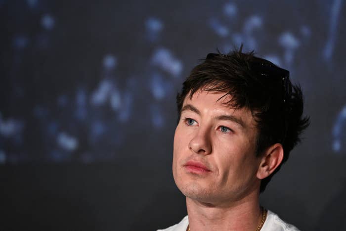 Barry Keoghan with short, tousled hair looks thoughtful in a candid moment at a press event