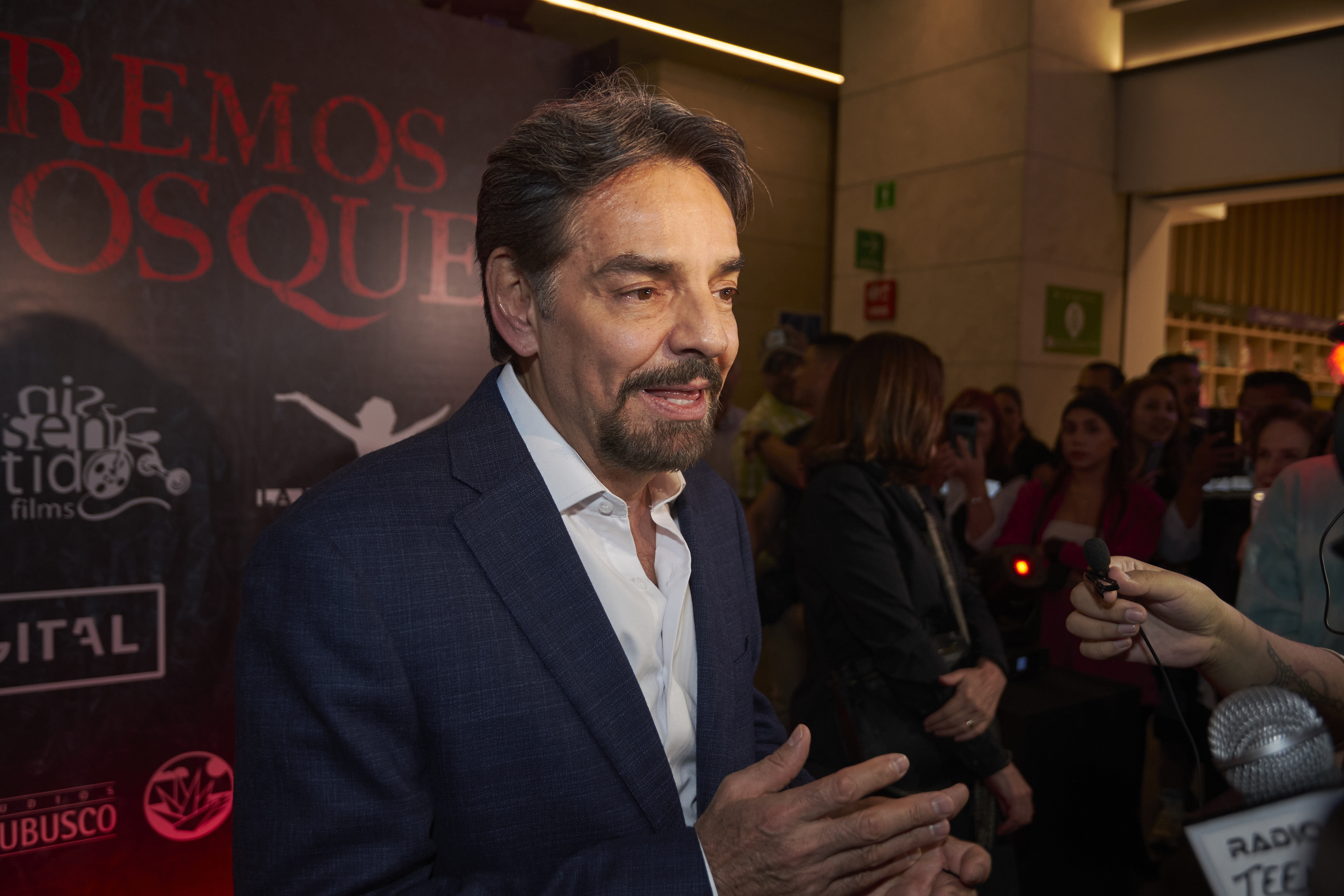 Eugenio Derbez in a suit speaks to journalists on a red carpet at a film event