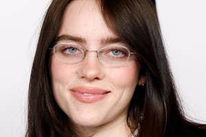 Billie Eilish wearing a suit with a tie and glasses, smiling at the camera
