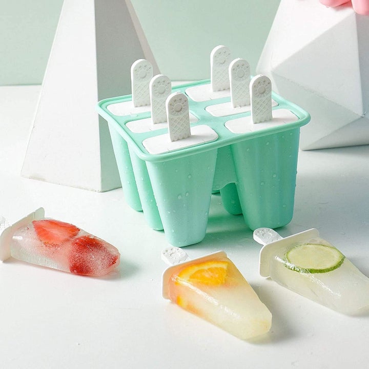 Ice pop molds with frozen fruit popsicles on a table, showcasing strawberries, lemon, and lime slices inside. Ideal for homemade summer treats