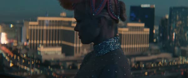 Pamela Anderson in profile wearing a beaded top and headband, with a city skyline in the background