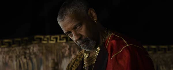 Denzel Washington  in ornate attire with gold accents gazes intensely. Background features intricate detailing, suggesting a dramatic or historical setting