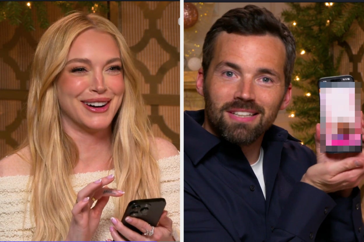 Two celebrities smiling, holding smartphones during an interview. The woman wears a stylish off-shoulder top, and the man holds a phone with the screen blurred