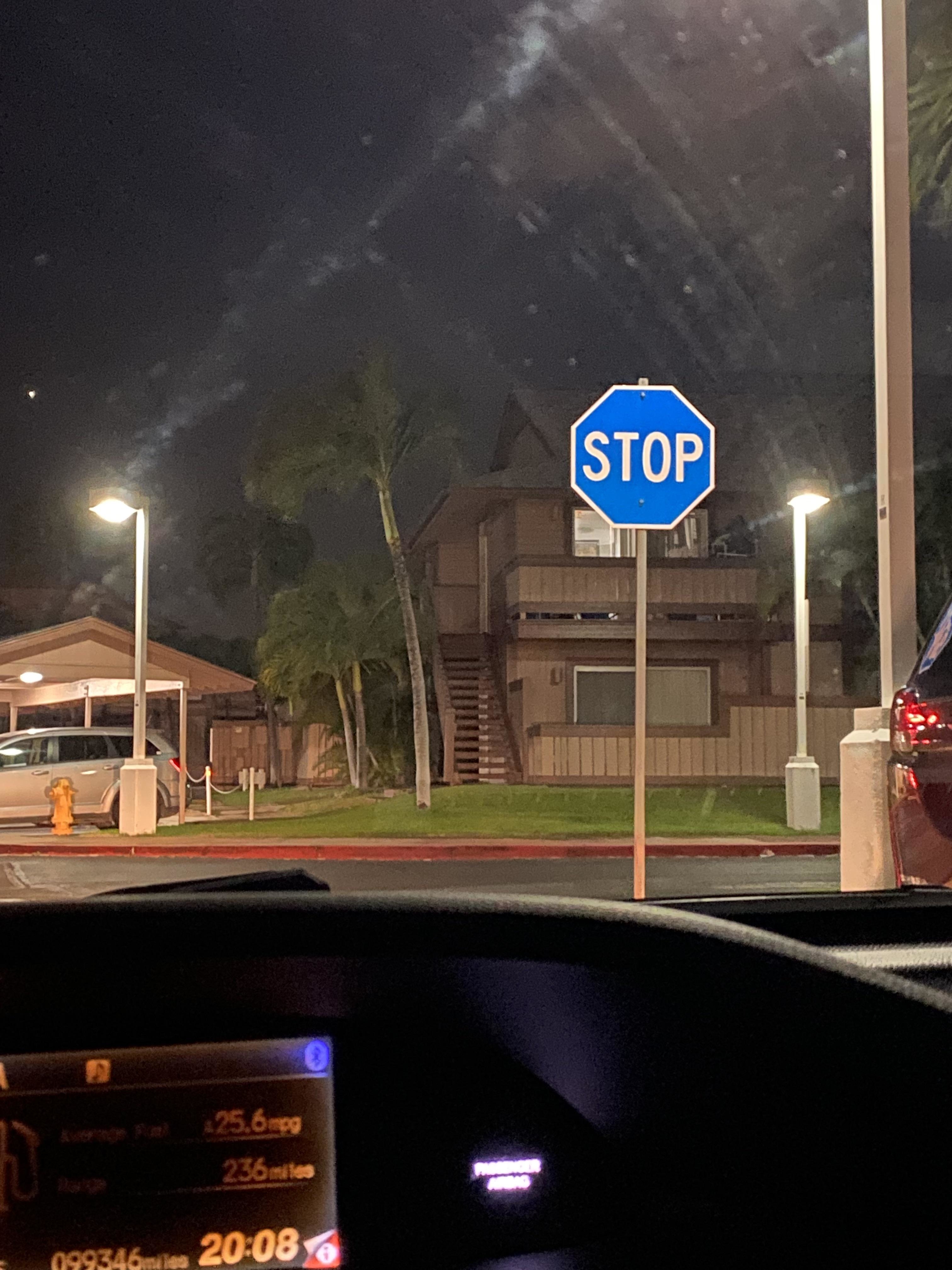 A stop sign is visible from a car windshield at night, in a residential area with a parked car and streetlights