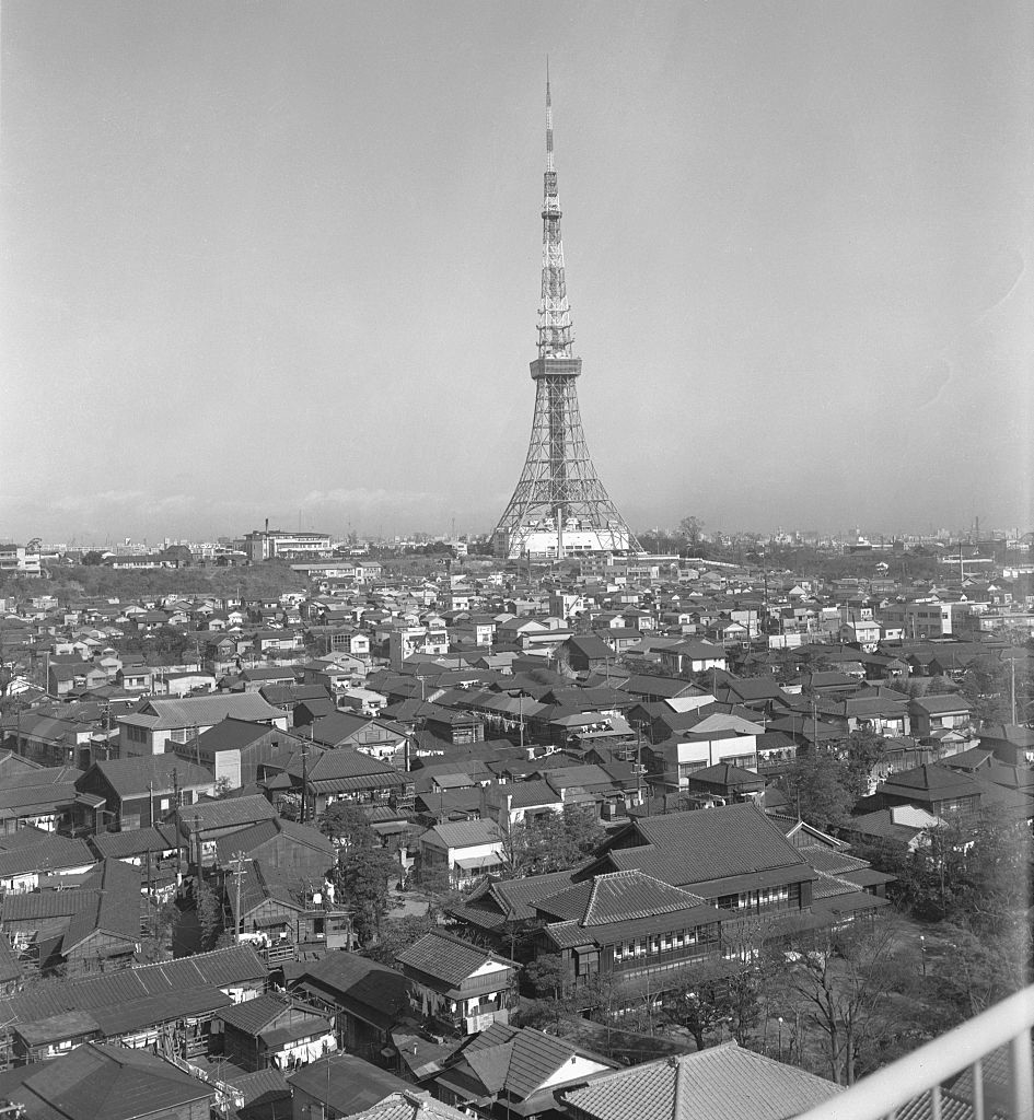 Black-and-white photo of Tokyo Tower rising above a sprawling cityscape with traditional Japanese buildings in the foreground