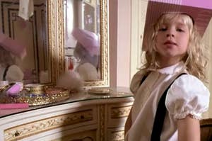 Child in vintage-style attire looking at a mirrored vanity with makeup items, reflecting a playful and nostalgic moment