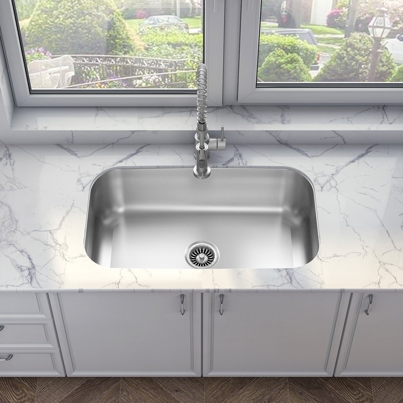 Modern kitchen with a stainless steel undermount sink set in a marble countertop, located beneath a large window with a view of a garden