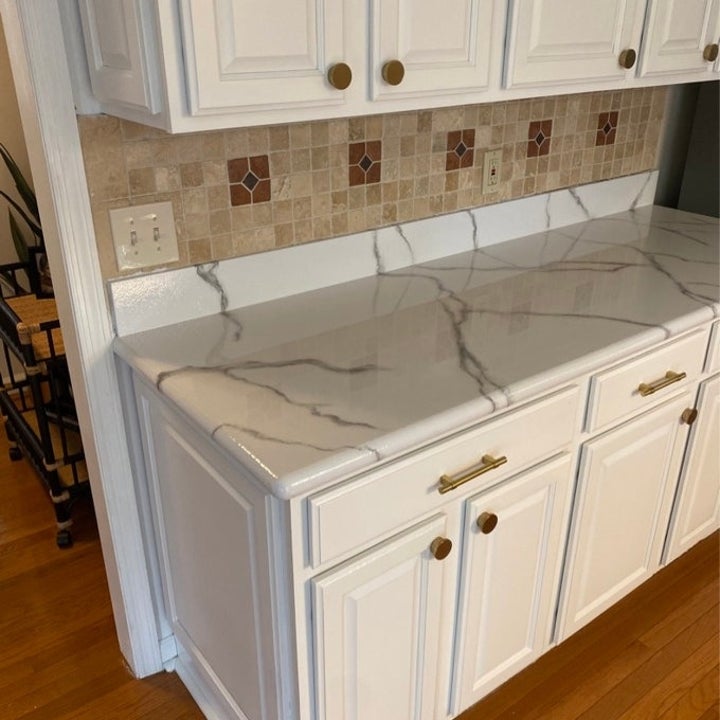 Marble-look kitchen countertop with brown veining, white cabinets with brass handles, and tiled backsplash