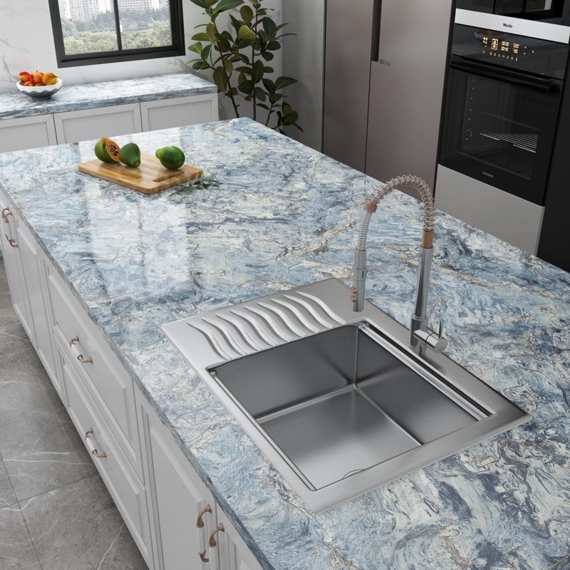 Modern kitchen with marble island, integrated stainless steel sink, and fruits on a cutting board; visible oven and potted plant