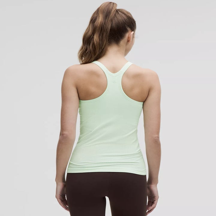 Different model wearing a light green racerback tank top and athletic leggings, shown from behind with their hair in ponytail