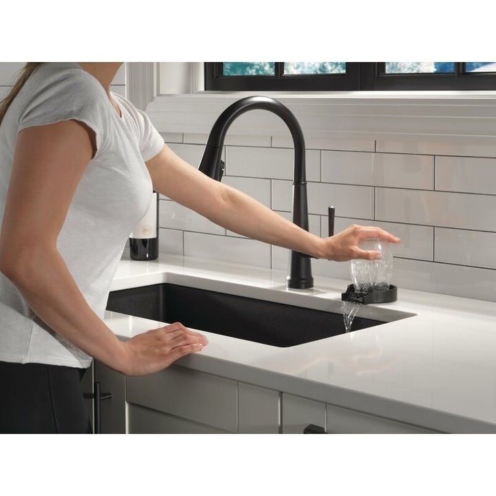 Person filling a glass at a modern kitchen sink with a sleek, black faucet, showcasing contemporary kitchen fixtures