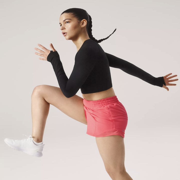 Person in activewear performs a running pose, wearing a black long-sleeve top and pink running shorts