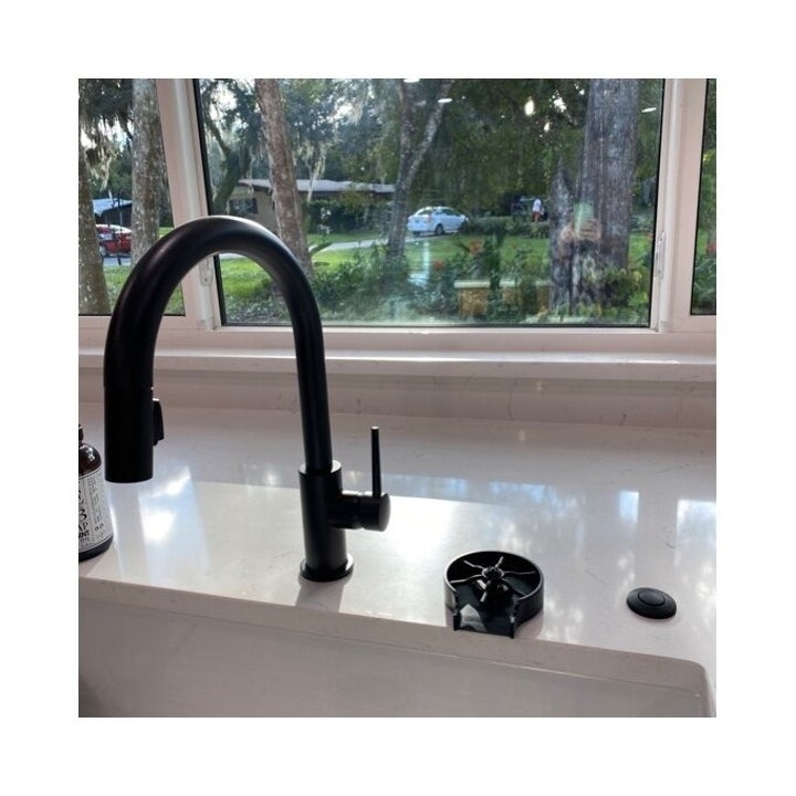 Modern kitchen sink with black faucet and soap dispenser, set against a bright window view of trees outside