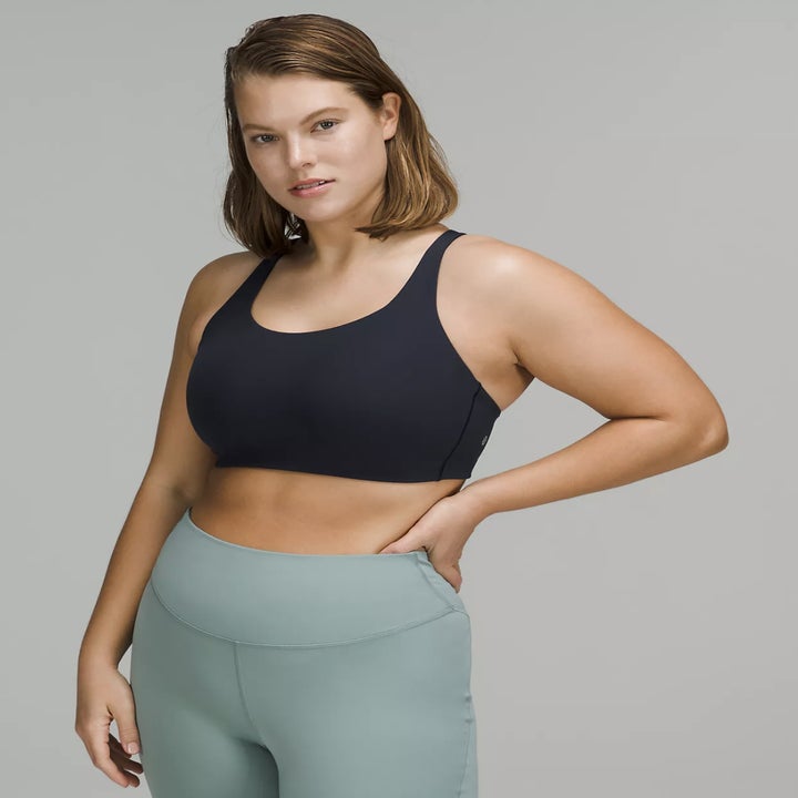 A model wearing a black sports bra and high-waisted workout leggings, posing with one hand on their hip
