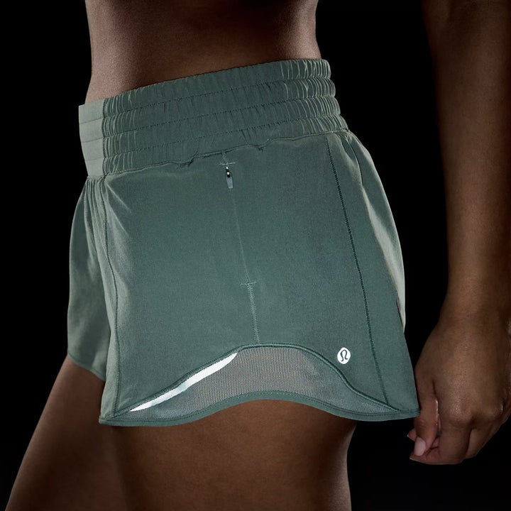 Close-up of someone wearing green sporty, fitted shorts with a small Lululemon logo in dark setting