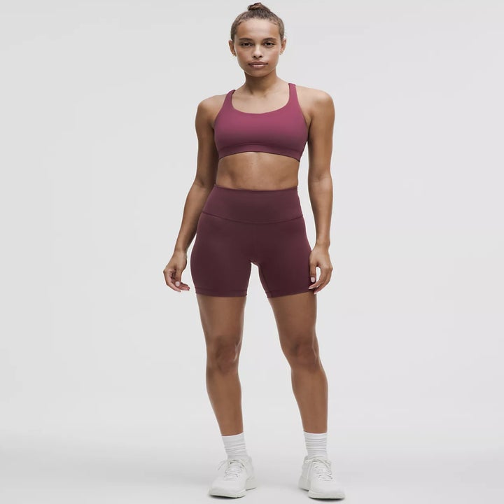 model wearing maroon sports bra and shorts, stands with neutral expression