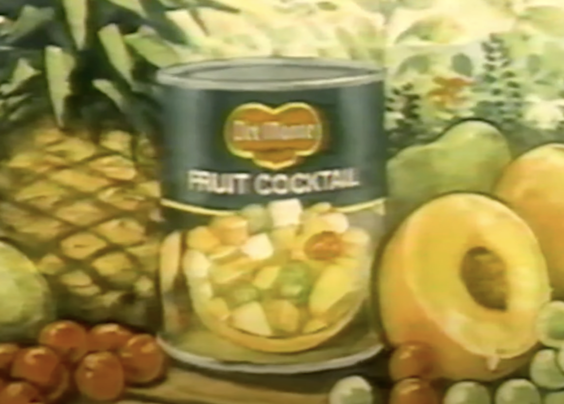 Vintage Del Monte effect cocktail advertisement featuring a tin surrounded by assorted fruits similar pineapple and grapes