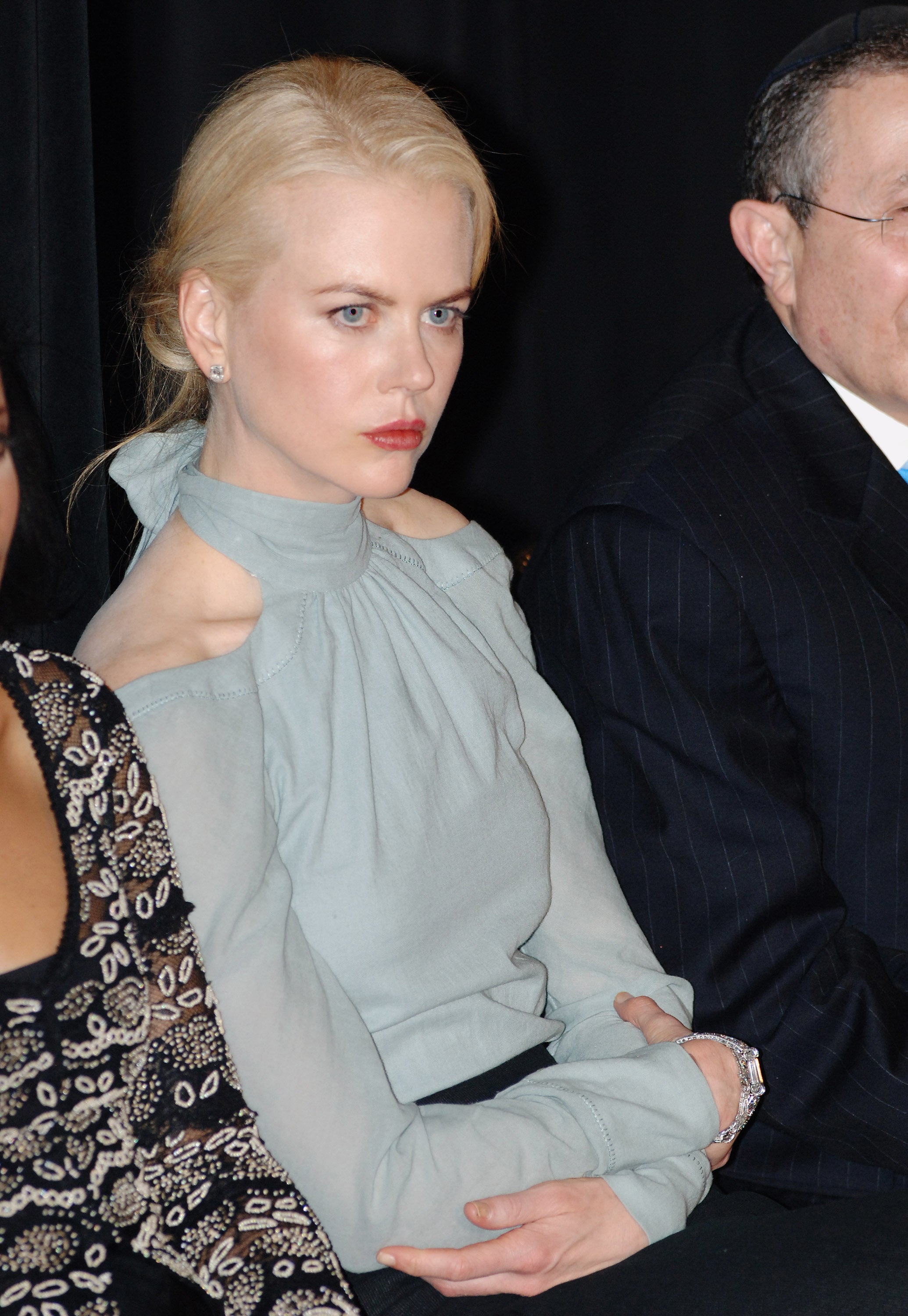 Nicole Kidman seated, wearing a stylish off-shoulder top, looks attentively forward