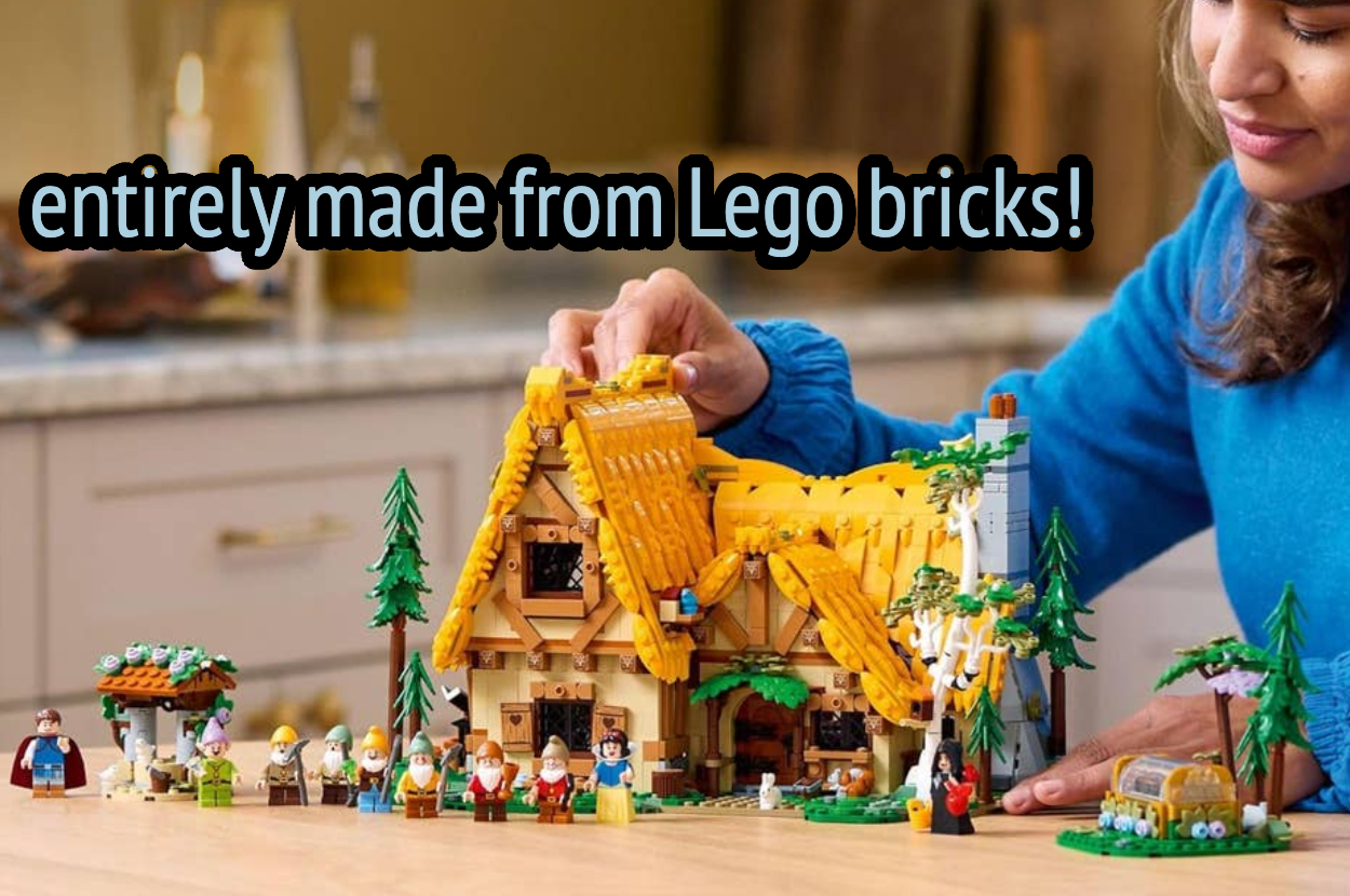 A person assembling a detailed Lego model of a cottage, surrounded by small Lego figures and trees, on a kitchen counter